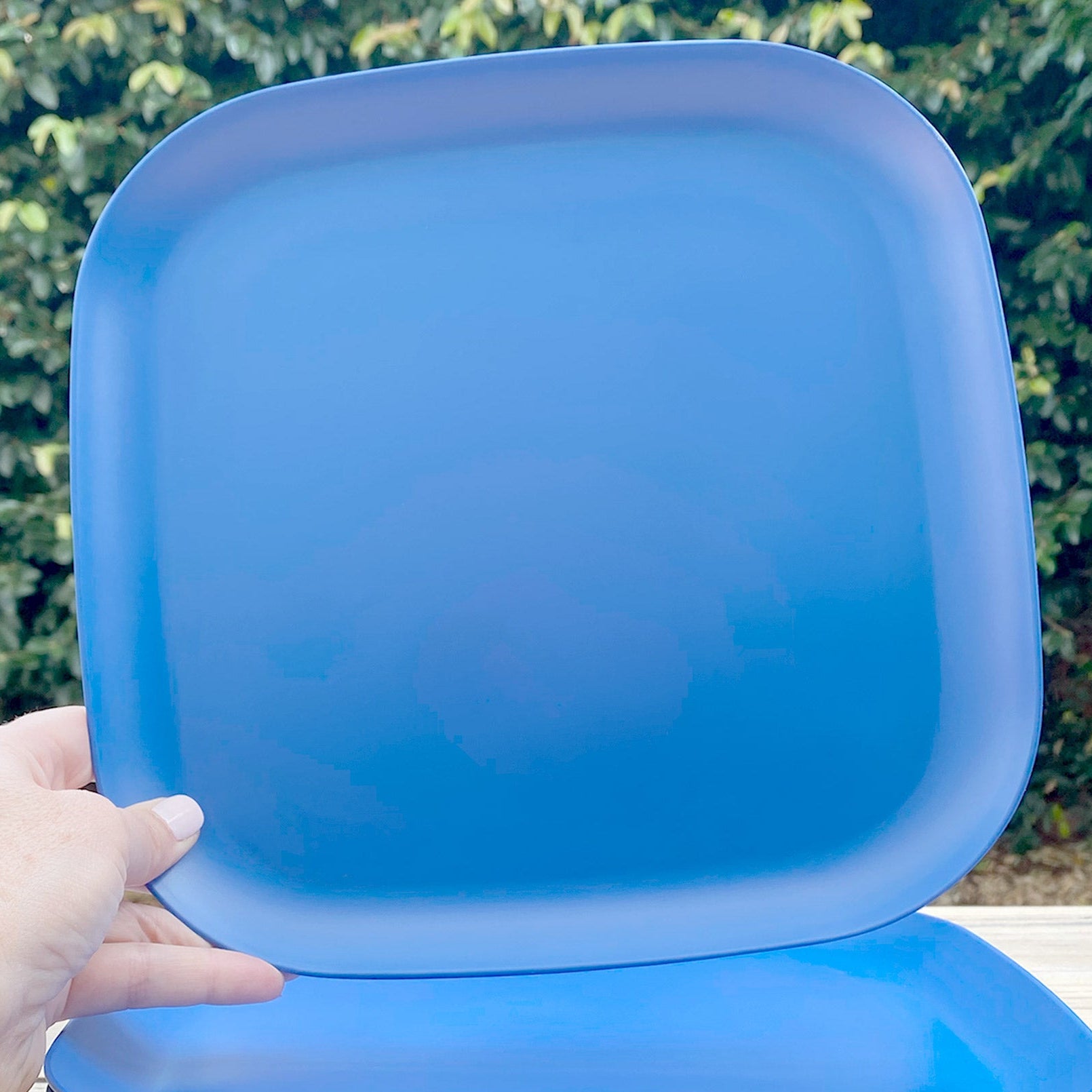 Stack of blue square plates on a wooden board with a hand holding the top plate.