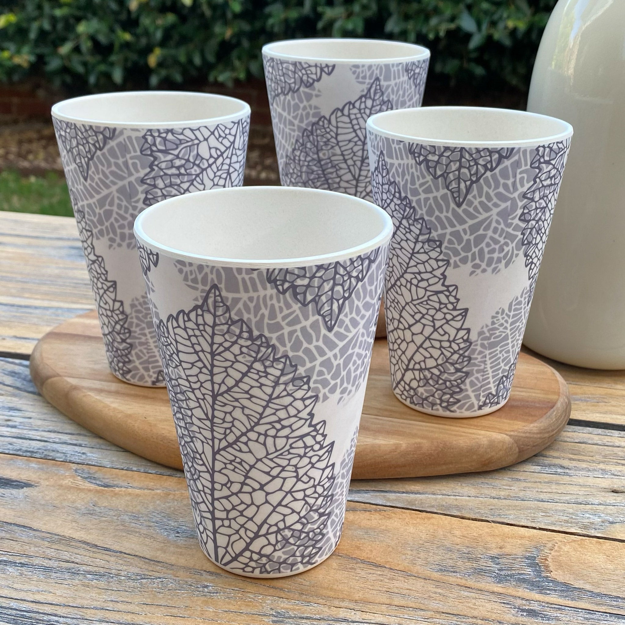 Four bamboo cups with leaf pattern on a wooden coaster outdoors