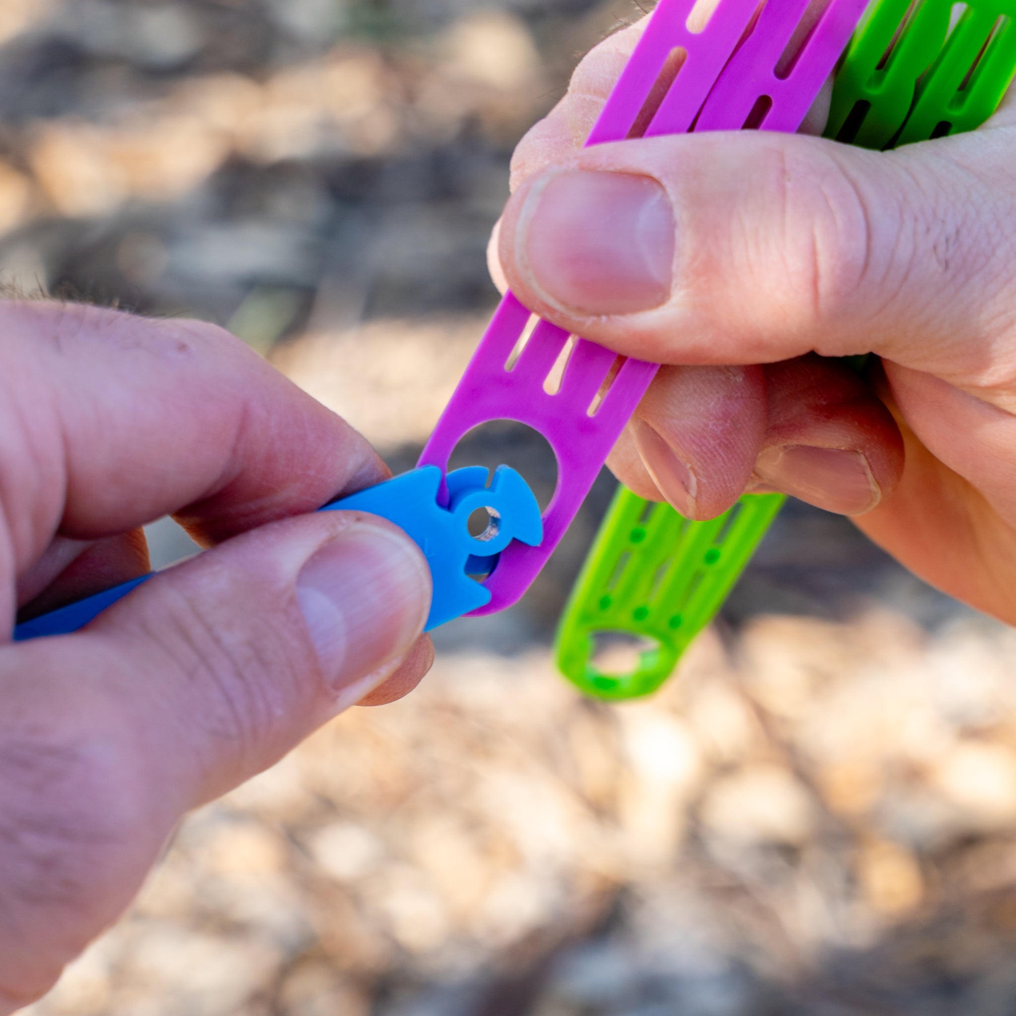 Close-up of hands holding Slide n' Dry rainbow pegless clothesline slides clicked together showing gripping slots