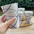 Hand holding a white ceramic cup with circles patterns on a wooden surface outdoors.