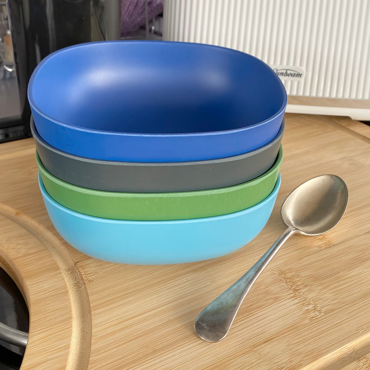 4 piece bamboo cereal bowl set, high country mix in classic green, midnight grey, pale blue and sea blue, on table with spoon