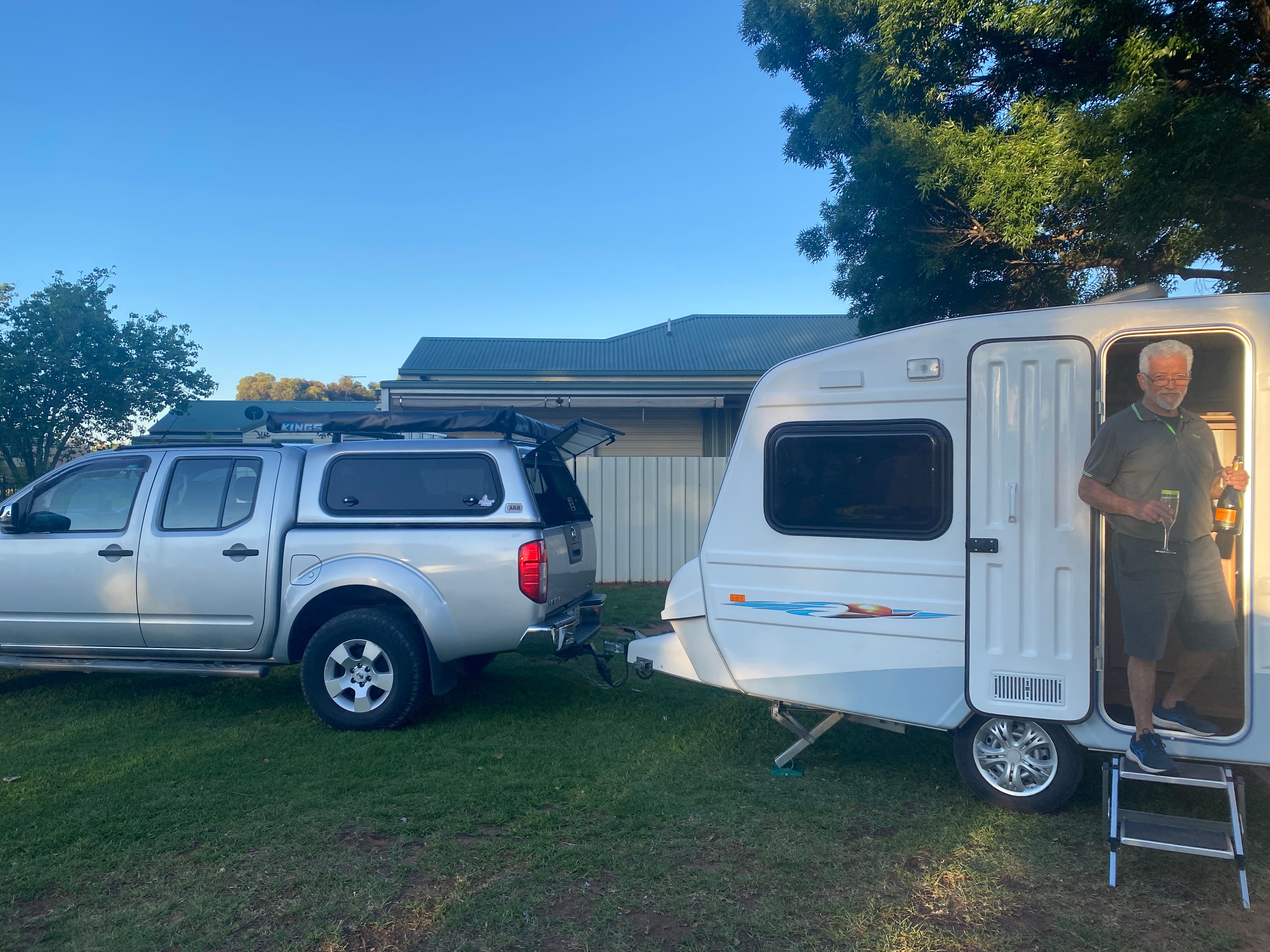 A silver 4 door canopy ute towing a Euro Hobby Caravan wtih a man exiting holding a champagne bottle and glass.