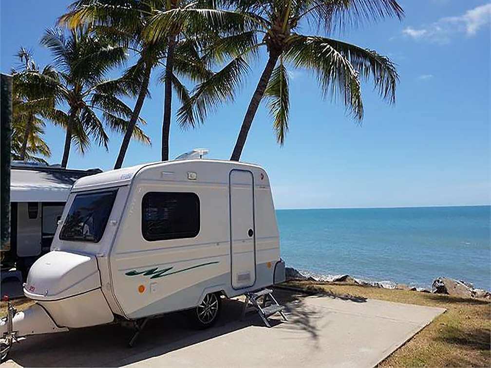 White Euro Hobby Caravan parked at camp site under palm trees with the sea behind.