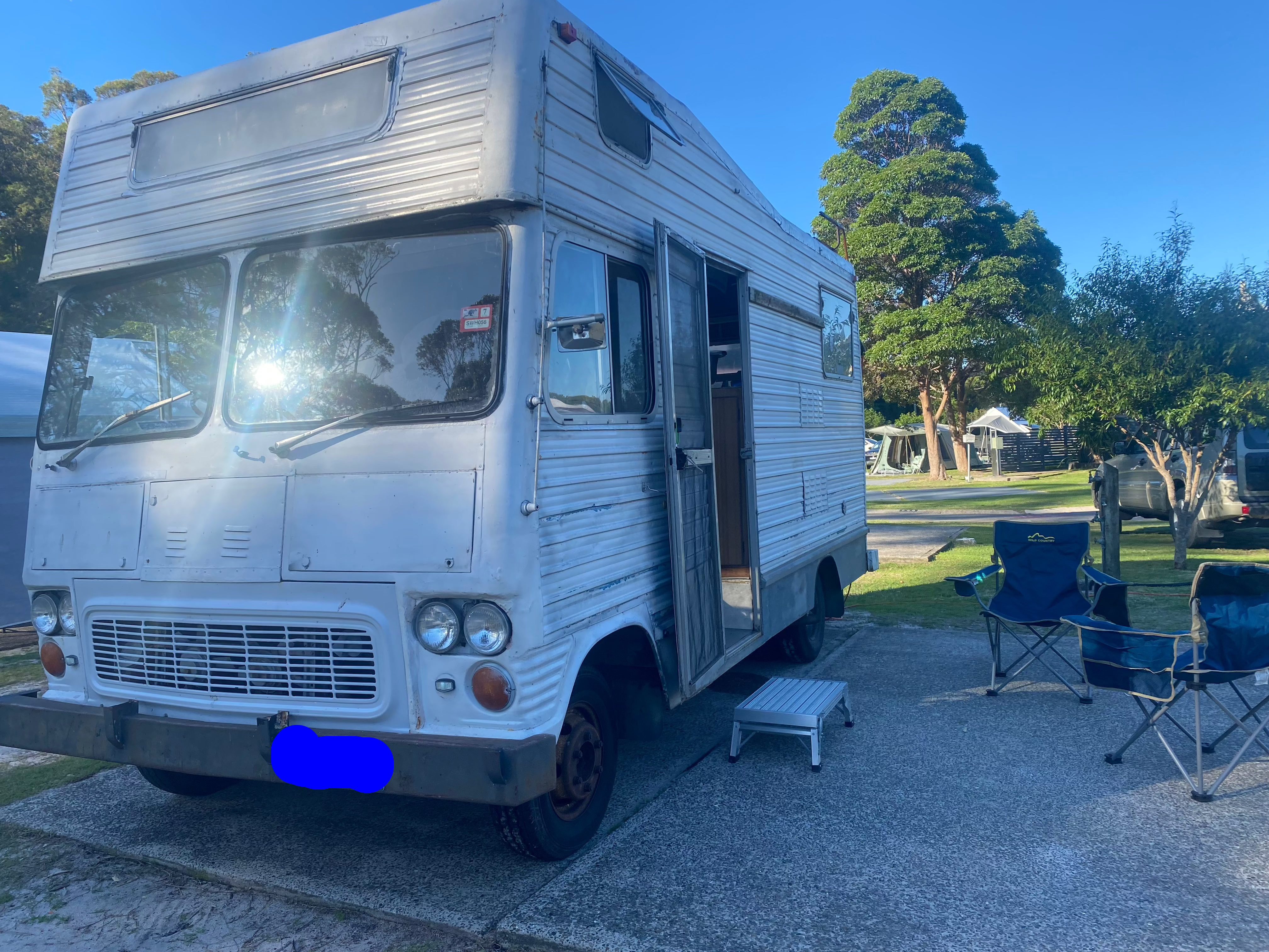 The Trusty Winnie-Bago Camper Van parked at a camp site with 2 blue fold out camp chairs.